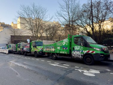 Paris, Fransa-23.02.2025 Canlı bir grafiti gösterisi sabahın erken saatlerinde çıplak ağaçlarla çevrili sakin bir şehir merkezinde park edilmiş yeşil taşıma araçlarını dekore ediyor..