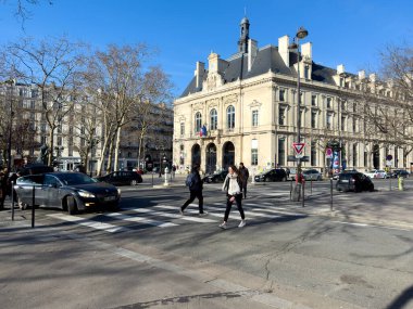 Paris, Fransa-23.02.2025 yayalar, Paris 'te güneşli bir günün canlı atmosferini gözler önüne sererek arka planda büyük tarihi bir yapıyla hareketli bir yaya geçidinde yol alırlar..