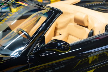 Paris,France-09.02.2025 A stunning black convertible with a tan leather interior is positioned elegantly amidst the colorful displays of a vintage auto exhibition, exuding luxury and nostalgia. clipart