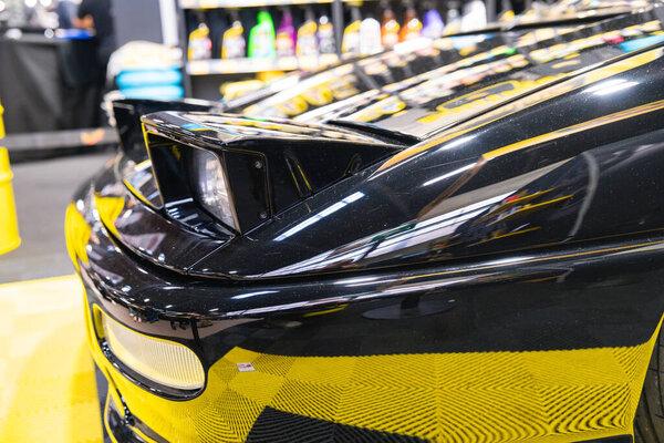 Черный спортивный автомобиль с отполированной поверхностью и аэродинамическим дизайном под яркими огнями представлен на оживленной автомобильной выставке..