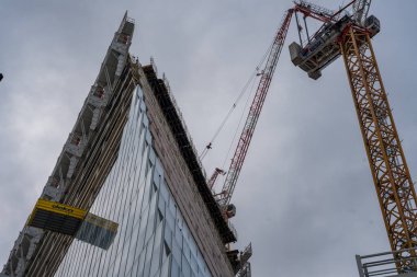 Paris, Fransa-09.02.2025 Bulutlu gökyüzünün ortasında, inşaat işçileri modern bir gökdelen üzerinde çalışarak, kentsel kalkınma ve takım çalışmalarını vurgulayarak ustalıkla kule vinçleri çalıştırıyorlar..