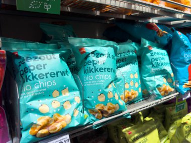 Paris, Fransa-25.02.2025 Alışverişçiler, sergilenen eşsiz ve cezbedici lezzet çeşitlerini sergileyen parlak abur cubur paketleriyle dolu yerel bir marketi keşfediyorlar..