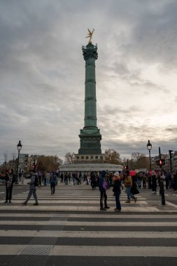Paris, Fransa-23.11.2024 kasvetli bir gökyüzü altında, insanlar tarihi Bastille sütunu yakınında karşıdan karşıya geçip alacakaranlık saatinde Paris 'in canlı enerjisini yakalıyorlar..