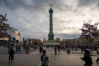 Paris, Fransa-23.11.2024 Paris 'teki Bastille Anıtı' nın etrafında canlı bir kalabalık toplanıyor. Sonbahar gökyüzü renklerin bir karışımını sergiliyor..
