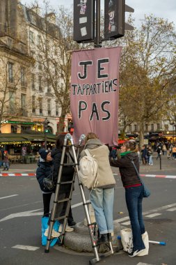 Paris, Fransa-23.11.2024 Tutkulu bir grup aktivist ağaçlar ve kafelerle dolu canlı bir şehir ortamında mülkiyete karşı cesur bir pankart asmak için bir merdiven kullanıyor..