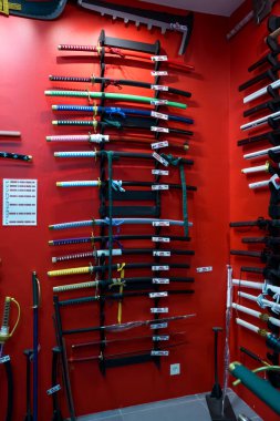 Paris, Fransa-23.11.2024 Bir dizi kılıç çeşitli renklerde ve tasarımlarla donatılmış cesur kırmızı bir duvar, her bir silahın ustalığını özel bir mağaza ortamında sergiliyor.