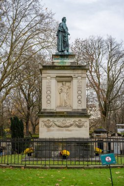 Paris, Fransa-23.11.2024 Sakin bir parkta heykel üzerinde duruyor, çıplak ağaçlar ve sonbahar yapraklarıyla çerçevelenmiş, bulutlu bir öğleden sonra barışçıl bir aura çağrıştırıyor.