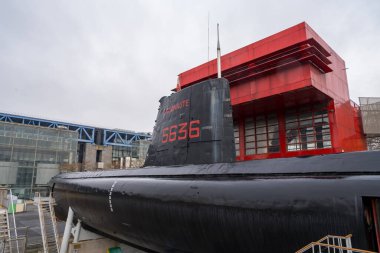 Paris, Fransa-03.12.2024 çağdaş binaların arkaplanının ortasında bir denizaltı, bulutlu bir günde endüstriyel manzarayla çelişen parlak yapısıyla gururla rıhtımda duruyor..