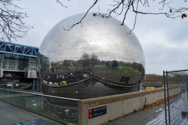 Paris, Fransa-03.12.2024 Ağaçlar ve binalar da dahil olmak üzere büyük metalik bir küre, şehirde bulutlu bir günde çarpıcı bir görsel etki yaratır..
