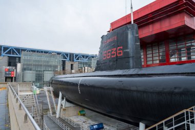 Paris, Fransa-03.12.2024 Ziyaretçiler, tarihsel deniz teknolojisi ve modern mimari arasındaki zıtlığı vurgulayarak, çağdaş bir yapının yanında demirlemiş dikkate değer bir denizaltıyı keşfediyorlar..