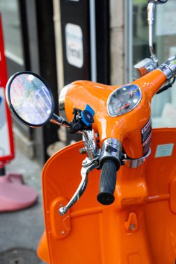 Paris, Fransa-20.20.2024 Parlak renkli turuncu bir scooter, parlak gidonu ve aynaları etrafındaki canlı atmosferi yansıtırken canlı bir şehir caddesinde parlıyor..
