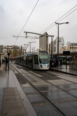 Paris, Fransa-03.12.2024 Modern bir tramvay yaklaşırken durakta bekleyenler serin ve bulutlu bir öğleden sonra Paris 'in hareketli sokaklarında zikzak çiziyorlar..