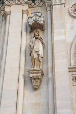 Güzel oyulmuş taş bir heykel katedrallerin ön cephesinde belirgin bir şekilde duruyor, gün batımının ılık renklerini yakalıyor ışık onun karmaşık ayrıntılarını aydınlatırken..