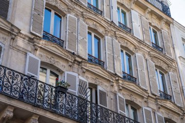 Bu büyüleyici cephe klasik Paris tasarımını gösteriyor, süslü pervazlar, kepenkli pencereler ve işlenmiş demir balkonlar, hepsi sıcak öğleden sonra ışığı altında parlıyor..