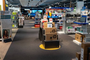 Chambourcy, France-09.03.2025 Alışverişçiler, parlak ışıklar altında düzenlenmiş kutular ve ürünlerin sergilendiği, çeşitli cihazlarla dolu şık bir teknoloji mağazasında geziniyorlar..