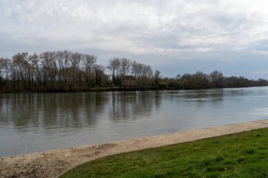 Sakin nehir boyunca hafif dalgalar hareket ediyor ağaçlar kıyılarda nöbet tutuyor ve bulutlu bir öğleden sonra La Roche-Guyon 'da sakin bir atmosfer yaratıyor..