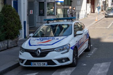 Kalabalık bir caddenin kenarına park etmiş bir polis arabası, şehirde aydınlık bir öğleden sonra halkın güvenliğini sağlamada kolluk kuvvetlerinin rolünü gösteriyor..