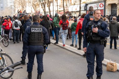 Kentsel bir alanda büyük bir kalabalık toplanırken, polis memurları çeşitli katılımcıların kaygılarını dile getirdikleri etkinliği izliyorlar..