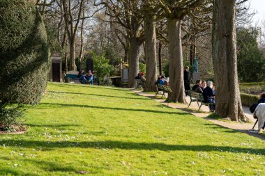 Paris, Fransa-02-03-2025 Ziyaretçiler, Pere Lachaise 'in yemyeşil bahçesinde toplandılar. Gün ışığı ağaçların arasından süzülüp, yansımaları ve sohbetleri davet ederken sakin bir öğleden sonranın tadını çıkarıyorlar..