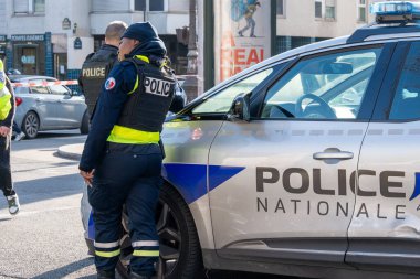 İki polis memuru kalabalık bir caddede devriye araçlarının yanında görev yaparken sivillerle etkileşime geçerek güvenlik ve toplum çatışmasını destekliyor..