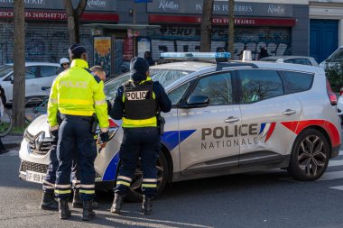 İki kolluk kuvveti memuru devriye arabalarında devam eden bir durumu tartışıyor ve canlı bir şehir ortamında halkın güvenliğine olan bağlılıklarını sergiliyorlar..