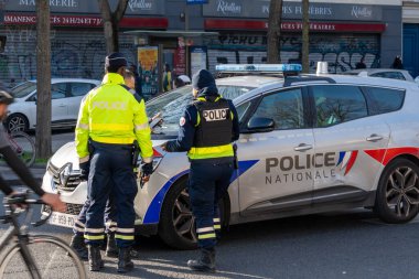 İki polis memuru kalabalık bir şehir caddesinde devriye arabalarının yanında iletişim kuruyor..