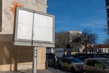 Kalabalık bir şehir caddesinin üzerinde beyaz boş bir ilan panosu beliriyor, park halindeki arabaların arasında rahatça yürüyen, şehir yaşamını ve çabukluğu ima eden.