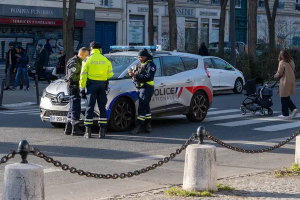 İki polis memuru, kalabalık bir caddede park halindeki bir polis aracının yanında vatandaşlarla etkileşime girerek, şehir güvenliği ve toplumsal çatışmanın özünü yakaladılar..