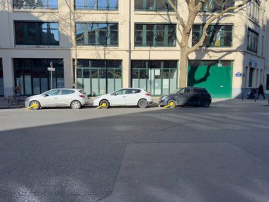 Paris, Fransa-02-03-2025 Üç park etmiş araç, güneşli bir günde, parlak sarı tekerlek kilitleri tarafından engellenir..
