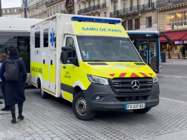 Canlı bir Paris meydanında toplu taşıma aracının yanında canlı bir ambulans bekliyor, bulutlu bir günde şehrin acil durum için hazır olduğunu gösteriyor..
