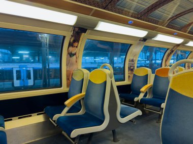 Paris, Fransa-28-02-2025 Modern bir trenin içinde, boş mavi ve sarı koltuklar büyük pencerelerden süzülen yumuşak ışık gibi konfor sunuyor..
