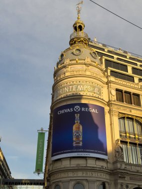 Paris, Fransa-04.03.2025 Şatafatlı bir bina çarpıcı bir reklamla süslenmiş. Şehir hayatının canlı enerjisini gün batımında yakalıyor..