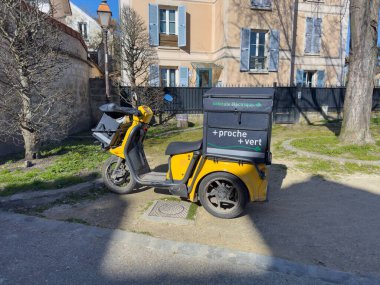 Villennes-sur-Seine, Fransa-06-03-2025. Parlak sarı bir elektrikli scooter, güneşli bir alanda park halinde duruyor. Bahar mevsimi taze yeşillik ve sükunet getirir..