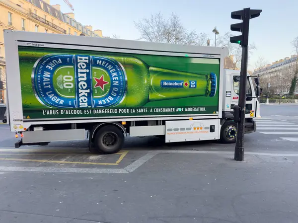 Paris, Fransa-07-03-2025 Bir dağıtım kamyonu öğleden sonra güneşinin altında yoğun bir kavşaktan geçiyor, yayaların dikkatini çeken renkli içecek markalarının yer aldığı.