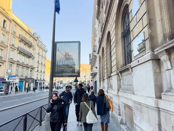 Paris, Fransa-07-03-2025 Çok çeşitli bir grup insan, sıcak havayı ve canlı atmosferi kutlarken aynı zamanda bir tiyatro reklamının önünden geçiyor..