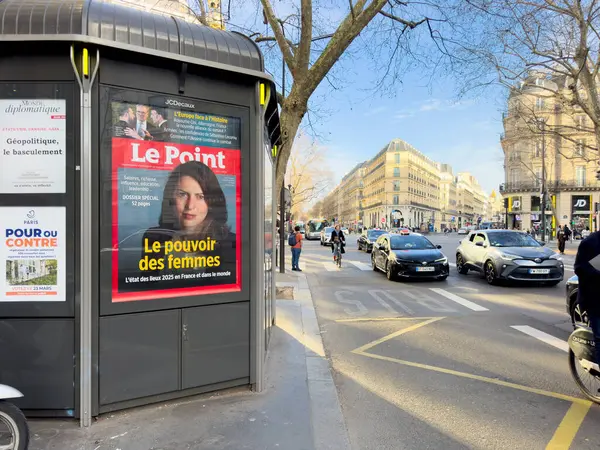 Paris, Fransa-07-03-2025 Parlak güneş ışığı Paris 'in işlek bir caddesini aydınlatıyor, kadınların güçlendirilmesi ile ilgili bir dergi kapağı sergileniyor, yayaların ve sürücülerin dikkatini çekiyor..