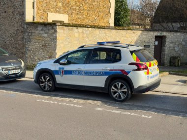 Villennes-sur-Seine, Fransa-08-03-2025 Bir belediye polis arabası, tuhaf bir Fransız kasabasının kaldırım taşı sokağının yanında park edilmiştir. Ağaçlar hafifçe sallanırken güneş, dingin çevreyi aydınlatır..