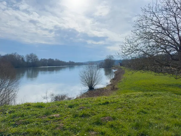 Sakin sular parlak bir gökyüzünün altında parıldıyor. Hafif meltemler ağaçların arasından süzülüp nehir kıyısına süzülürken ilkbaharın başlarında sakin bir kaçış yaratıyor..