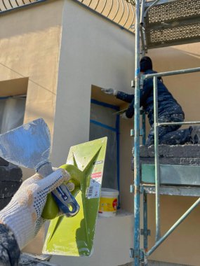 Villennes-sur-Seine, Fransa-15.03.2025 İşçiler, açık mavi gökyüzü altında iskele ve araçları ustalıkla kullanırken, bir binanın dış duvarını dönüştürmekle meşguller..