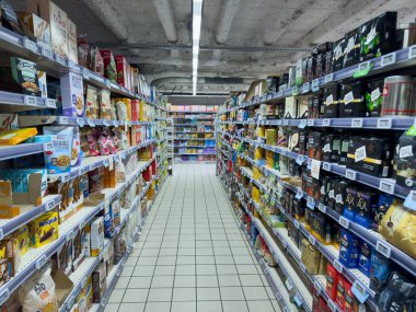 Paris, Fransa-16-03-2025 Alışverişçiler, parlak ışık altında gevrek, abur cubur ve çeşitli ev eşyaları paketleriyle çevrili, iyi organize edilmiş bir market koridorunda dolaşıyorlar..