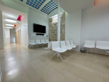 Paris, Fransa-21-03-2025 parlak ışıklandırılmış bekleme salonu taş bir duvarın etrafına yerleştirilmiş parlak, beyaz koltuklar içeriyor. Renkli aksanlar ziyaretçiler için bu sakin, davetkar alana hayat katıyor.