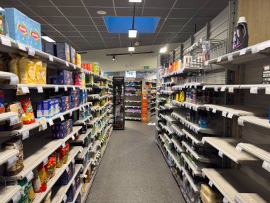 Villennes-sur-Seine, Fransa-01.03.2025 rafları çeşitli yiyecek ve ev eşyalarıyla dolu ve sakin bir öğleden sonra yerel bir markette seyrek bir seçim gösteriyor. Alışverişçiler azdır, dikkat çekerler