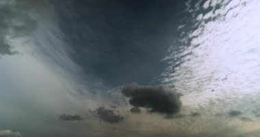 Gökyüzünün açık mavi şeritli zaman çizelgesi beyaz yüksek seviye sirostratus bulutlarıyla sınırlıdır ve koyu gri alt seviye kümülüs bulutları hareket eder ve şekil değiştirir.