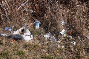 Çöp, (görünmeyen) bir şehir deresinin yanında çimenli bir alan boyunca atıldı .