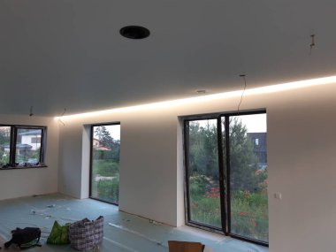 Tadilat sürecinde gibi görünen bir oda. Odada, duvarın üst kısmı boyunca uzanan ve yumuşak, dağınık bir parıltı sağlayan uzun bir LED şeridi var.. 