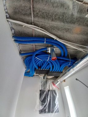 Bu resim, açıkta kalan HVAC bileşenlerine sahip bitmemiş bir tavanın yakın açılı ve düşük açılı görüntüsünü gösterir. Tavanın sert, beton gibi bir dokusu var. Bu da yapım aşamasındaki bir alanı işaret ediyor.. 