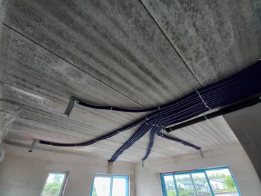 Bu resim, açıkta kalan HVAC bileşenlerine sahip bitmemiş bir tavanın yakın açılı ve düşük açılı görüntüsünü gösterir. Tavanın sert, beton gibi bir dokusu var. Bu da yapım aşamasındaki bir alanı işaret ediyor.. 