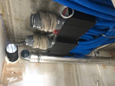 Bu resim, açıkta kalan HVAC bileşenlerine sahip bitmemiş bir tavanın yakın açılı ve düşük açılı görüntüsünü gösterir. Tavanın sert, beton gibi bir dokusu var. Bu da yapım aşamasındaki bir alanı işaret ediyor.. 