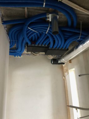 Bu resim, açıkta kalan HVAC bileşenlerine sahip bitmemiş bir tavanın yakın açılı ve düşük açılı görüntüsünü gösterir. Tavanın sert, beton gibi bir dokusu var. Bu da yapım aşamasındaki bir alanı işaret ediyor.. 