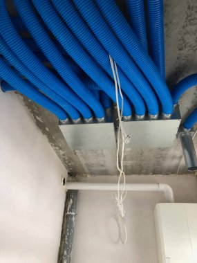 Bu resim, açıkta kalan HVAC bileşenlerine sahip bitmemiş bir tavanın yakın açılı ve düşük açılı görüntüsünü gösterir. Tavanın sert, beton gibi bir dokusu var. Bu da yapım aşamasındaki bir alanı işaret ediyor.. 